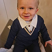 Augustin participe au concours pour gagner de l'argent avec cette photo : child, toddler, smiling, sitting, clothing, navy_sweater, white_collar, indoor, face, person, cute, happy, young_child, portrait, buttoned_shirt, chair, blanket, hand, light_skin, short_hair