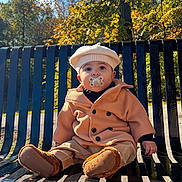 Dylan is registered to the contest to win money with this photo: baby, child, pacifier, coat, beret, bench, outdoor, autumn, fall, sunlight, park, leaves, nature, cute, sitting, footwear, warm_clothing, daytime, portrait, young