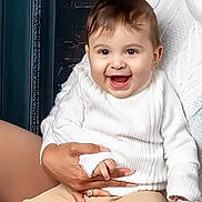 Dylan is registered to the contest to win money with this photo: baby, child, smiling, white_sweater, happy, person, portrait, indoor, holding, hands, cute, face, infant, apparel, sitting, light_skin, closeup, joy, warm, cozy