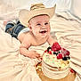 baby, cowboy_hat, cake, berries, cream, smiling, messy, blanket, jeans, happy, child, food, celebration, portrait, indoor, cute, dirt_on_face, sitting, playful, dessert