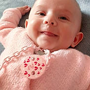 Liv a rejoint le concours — aidez-le/la à gagner de superbes lots ! baby, smile, pink_sweater, pacifier, chain, lying_down, cozy, blanket, face, tongue, cute, infant, child, soft_texture, warmth, indoors, happy, closeup, head, person