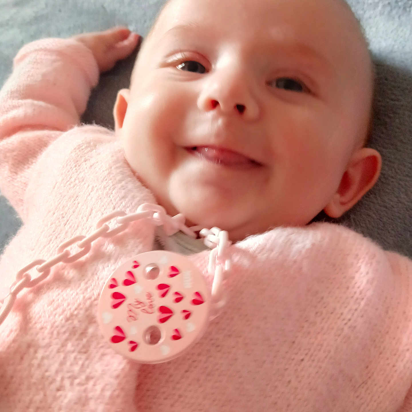 Liv a rejoint le concours — aidez-le/la à gagner de superbes lots ! baby, blanket, chain, child, closeup, cozy, cute, face, happy, head, indoors, infant, lying_down, pacifier, person, pink_sweater, smile, soft_texture, tongue, warmth