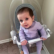 Isabella joined the competition — help win amazing prizes! baby, child, high_chair, purple_onesie, sitting, indoor, floor, tile_floor, wall, footrest, safety_bar, grip, curious, smiling, person, young_child, earrings, transparent_chair, modern_furniture, home