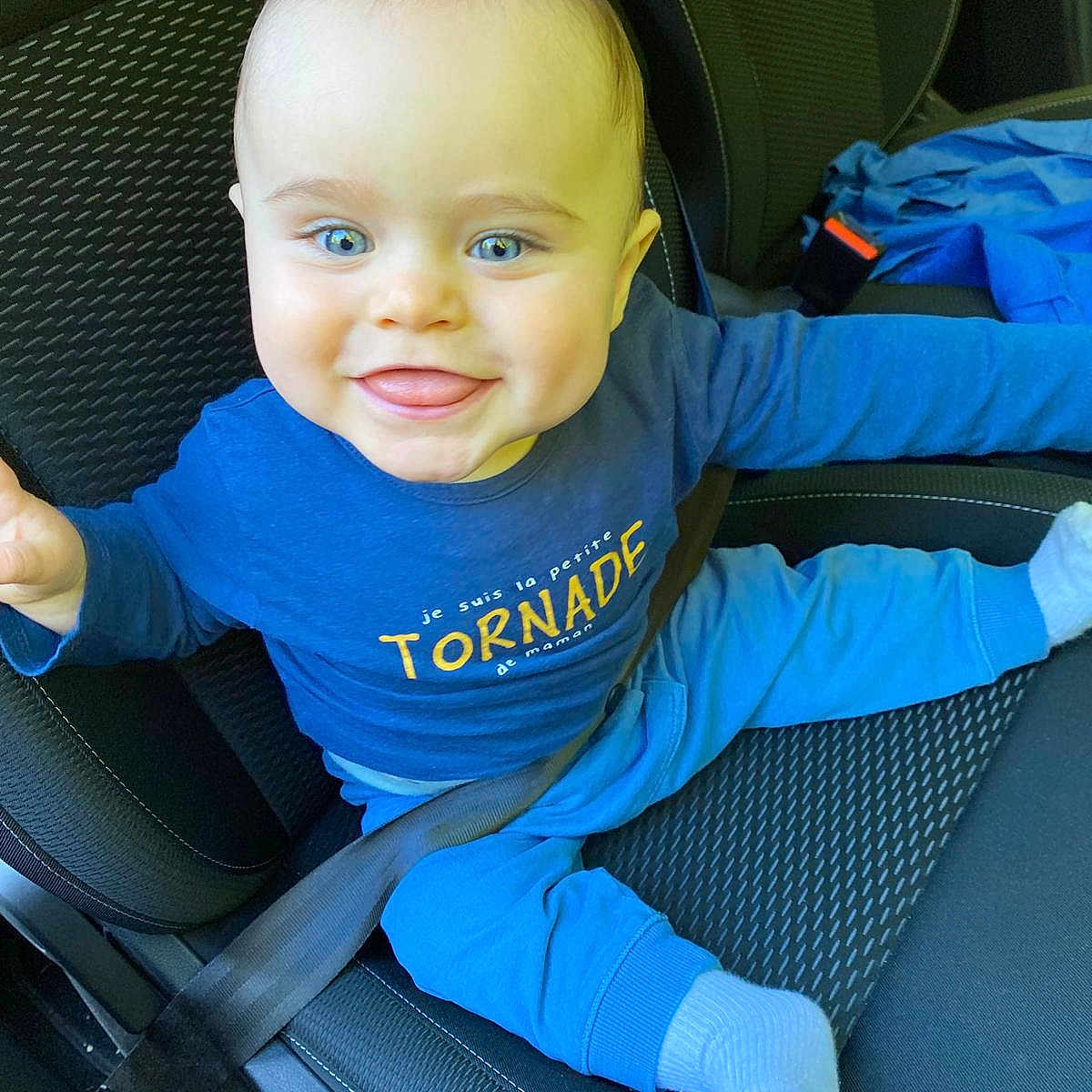 Ethan a rejoint le concours — aidez-le/la à gagner de superbes lots ! baby, blue_clothing, blue_eyes, car_seat, cheeks, child, cute, happy, head, infant, inside_car, jacket, person, seat, seatbelt, smiling, socks, text_on_shirt, tongue_out, young