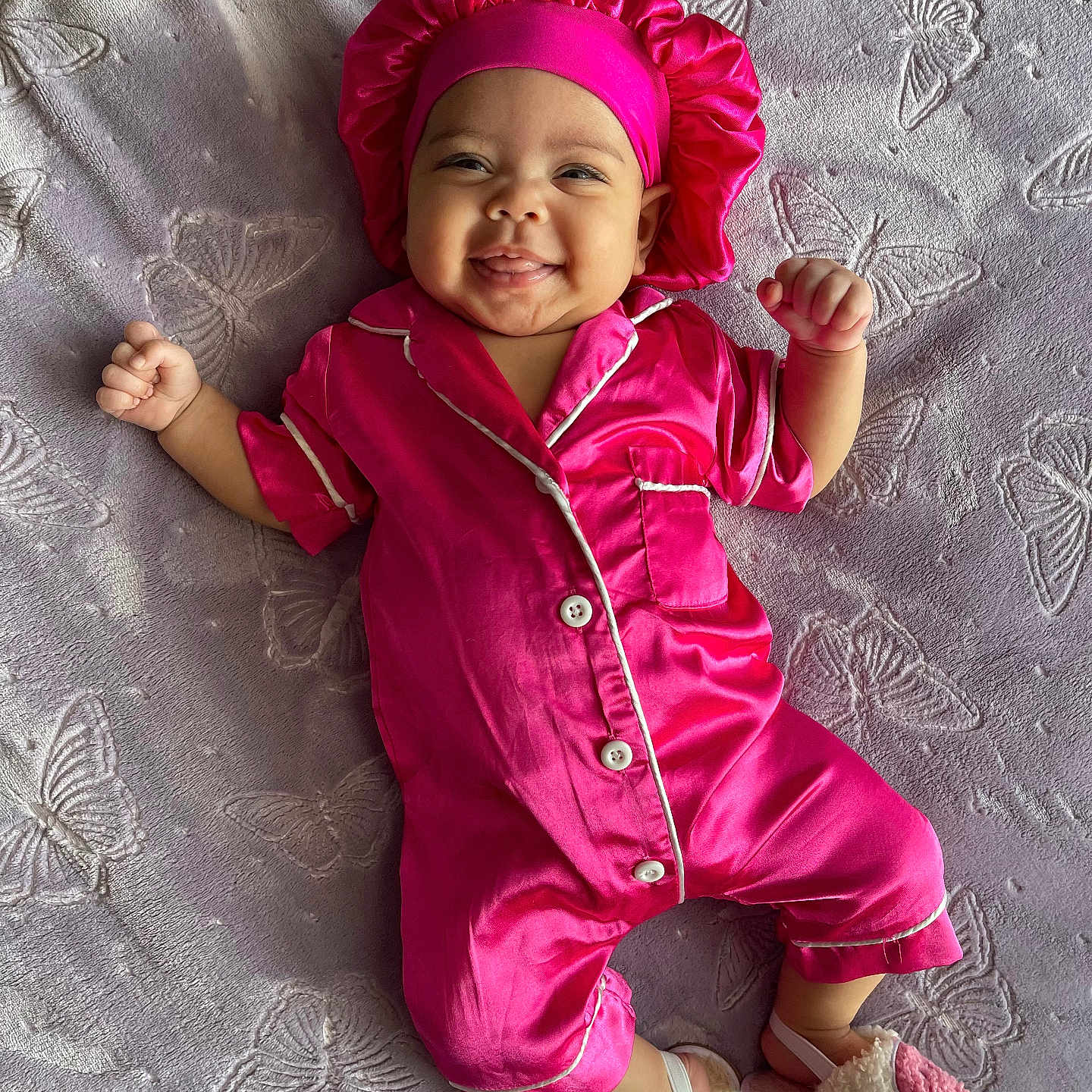Sayana is registered to the contest to win money with this photo: baby, blanket, bonnet, butterfly_pattern, child, comfortable, cozy, cute, footwear, happy, indoors, infant, lying_down, person, pink_pajamas, portrait, sleepwear, slippers, smile, soft_texture