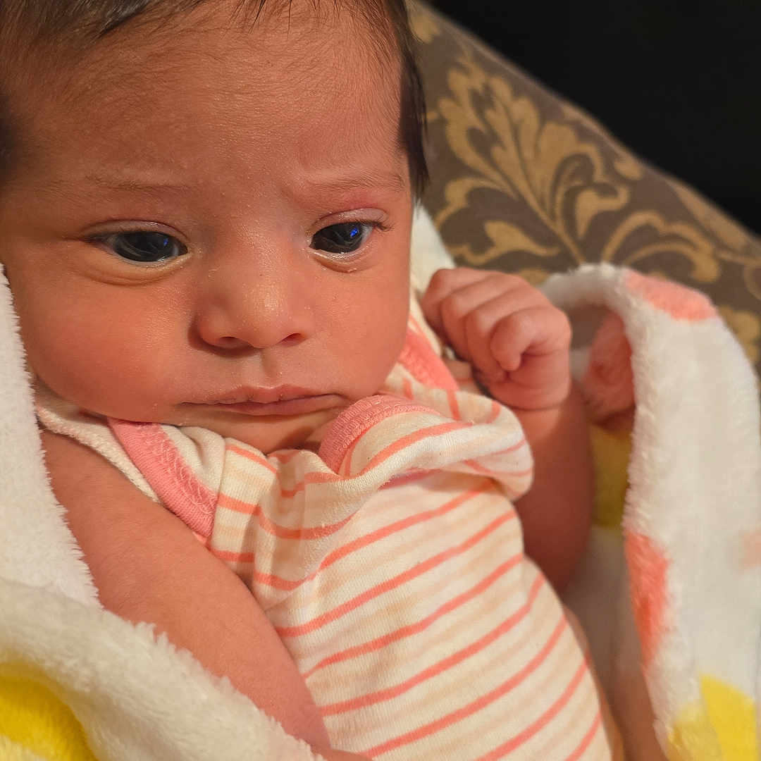 Adelyn joined the competition — help win amazing prizes! newborn, baby, infant, child, portrait, close_up, face, eyes, indoors, blanket, swaddle, onesie, striped_clothing, pink, cozy, lying_down, cushion, soft_lighting, sleeping_area, cute