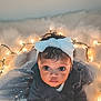 Caleigh is registered to the contest to win money with this photo: baby, child, infant, headband, bow, fairy_lights, fluffy, blanket, cute, portrait, indoors, soft_lighting, cozy, curious, hands, dark_hair, warm_tones, looking_up, clothing, toddler