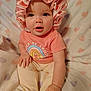 baby, child, clothing, cute, expression, face, footed_pants, hand, happy, heart_pattern, indoors, infant, pastel_colors, pink_bonnet, portrait, rainbow_shirt, sitting, smiling, soft_blanket, young_child