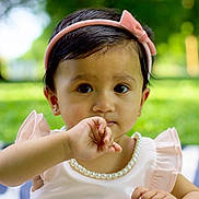 Prisha joined the competition — help win amazing prizes! toddler, child, girl, headband, pearl_necklace, pink_dress, outdoor, park, grass, blanket, portrait, cute, baby, sitting, hand, face, expression, nature, daylight, curious