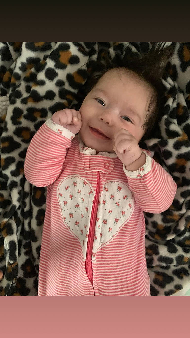 Julianna is registered to the contest to win money with this photo: arm, baby, baby_toddler_clothing, cheek, collar, dress, face, finger, gesture, head, joy, lip, nose, outerwear, person, pink, product, skin, sleeve, smile