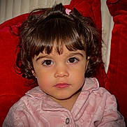 Caroline is registered to the contest to win money with this photo: child, toddler, face, portrait, brown_eyes, curly_hair, pink_jacket, clip, indoor, red_cushion, serious_expression, cute, young_child, person, closeup, warm_clothing, baby, sitting, eyelashes, indoors