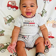 Psalm is registered to the contest to win money with this photo: baby, child, smiling, sitting, blanket, toy_pattern, shirt, shorts, sneakers, footwear, cute, happy, indoors, portrait, infant, person, new_balance, clothing, hand, face