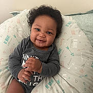 Princeton joined the competition — help win amazing prizes! baby, smiling, curly_hair, pillow, patterned, clothing, infant, happy, face, hands, sitting, indoors, cute, child, portrait, young, person, cozy, expression, comfortable