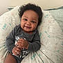 baby, smiling, curly_hair, pillow, patterned, clothing, infant, happy, face, hands, sitting, indoors, cute, child, portrait, young, person, cozy, expression, comfortable