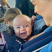 Isaïa a rejoint le concours — aidez-le/la à gagner de superbes lots ! baby, smiling, blue_eyes, baby_carrier, denim, adult, person, happy, close_up, face, child, holding, casual_clothing, indoor, people, parent, family, joy, cute, love