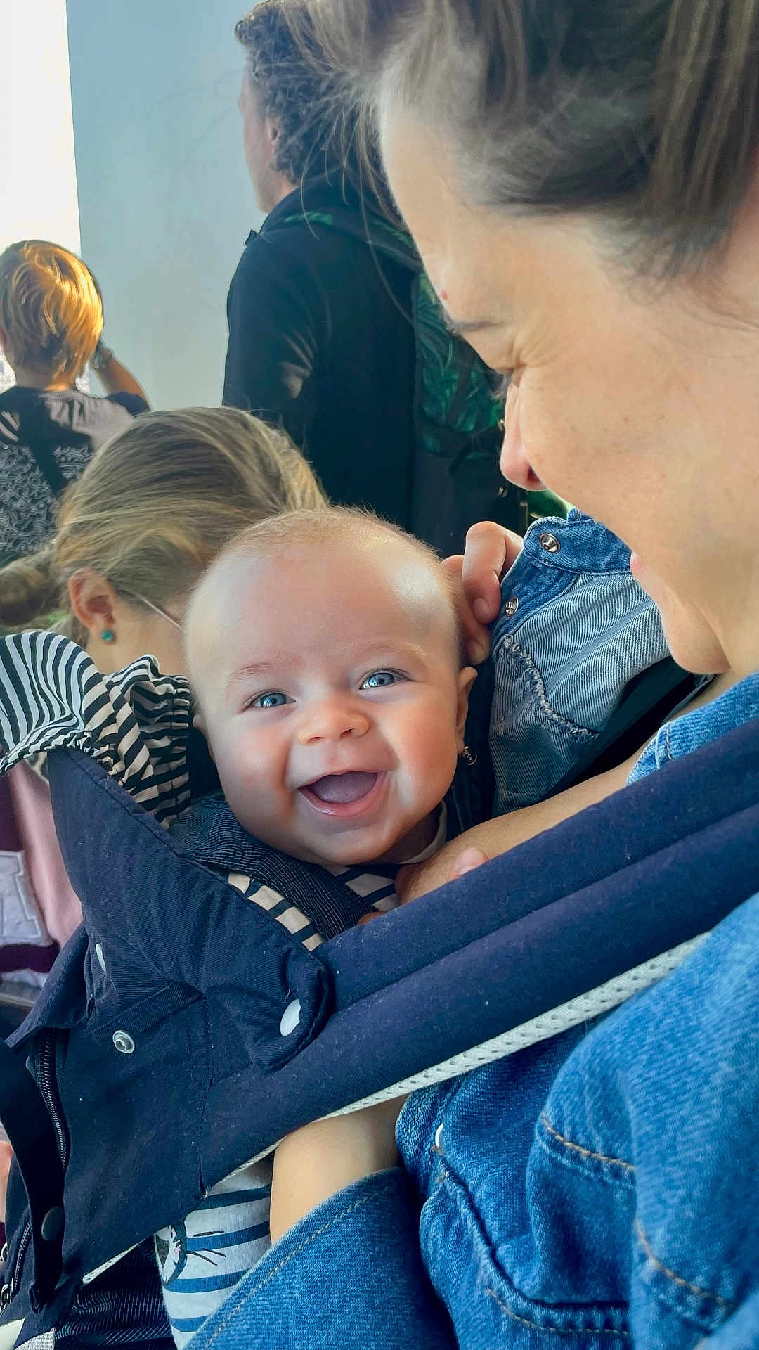 Isaïa a rejoint le concours — aidez-le/la à gagner de superbes lots ! baby, smiling, blue_eyes, baby_carrier, denim, adult, person, happy, close_up, face, child, holding, casual_clothing, indoor, people, parent, family, joy, cute, love