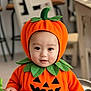 baby, pumpkin_costume, orange, green, cute, child, indoor, costume, halloween, smile, face, headwear, leaf, sitting, toy, person, infant, holiday, playful, adorable