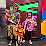 child, baby, toddler, person, group, family, glasses, tshirt, shorts, slippers, floor, indoor, colorful_background, holding_hands, smiling, standing, casual_clothing, halloween, bag, photography