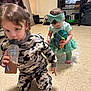 Odin is registered to the contest to win money with this photo: child, toddler, indoor, floor, toy, bottle, pajamas, headband, tutu, curly_hair, playing, kitchen, appliance, standing, kneeling, drink, carpet, cabinet, person, cute