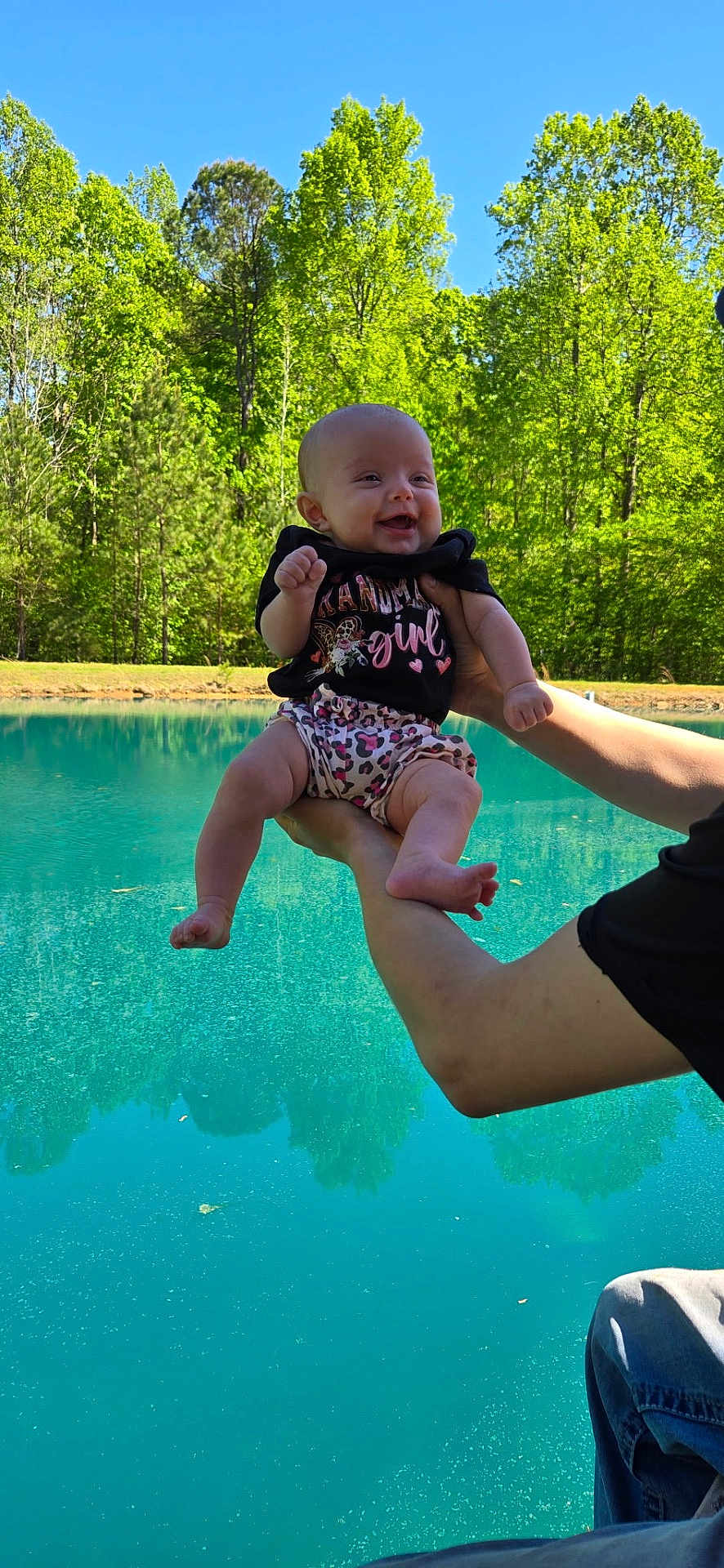 Sadie joined the competition — help win amazing prizes! baby, child, smiling, outdoor, pond, water, trees, greenery, person, holding, cute, nature, sunlight, happy, infant, clothing, shorts, tshirt, arms, legs