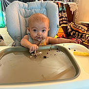 Sadie joined the competition — help win amazing prizes! baby, high_chair, messy, chocolate, cake, crumbs, face, hands, indoor, living_room, furniture, blanket, person, child, food, snack, cute, infant, seat, expression