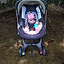 baby, car_seat, sunglasses, pink_bow, infant, outdoor, stone_wall, child, toy, footwear, seatbelt, sunlight, shadow, ground, wheels, stroller, cute, fashion, accessory, relaxing
