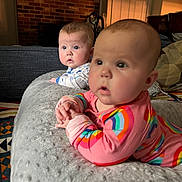 Olive is registered to the contest to win money with this photo: baby, infant, child, cushion, rainbow_clothing, onesie, face, blue_eyes, curious, indoor, home, fireplace, brick_wall, soft_lighting, carpet, blanket, pillow, person, cute, portrait