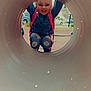 backpack, casual_clothing, child, circular, cute, daytime, denim, fun, happy, jeans, joyful, outdoor, park, person, playground, playing, smiling, star_effect, tunnel, young