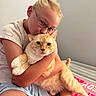 child, glasses, cat, orange_tabby, bed, blanket, hugging, affection, indoor, casual_clothing, shorts, short_sleeve_shirt, pet, domestic_animal, cute, love, face, person, resting, cozy