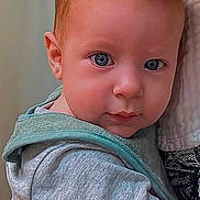 Sean joined the competition — help win amazing prizes! baby, infant, child, portrait, face, eyes, blue_eyes, red_hair, sitting, being_held, adult, clothing, gray_clothing, teal_clothing, indoor, close_up, looking_at_camera, serious_expression, soft_background, family