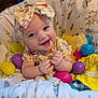 baby, smiling, headband, bow, plastic_eggs, colorful, blanket, plush_toy, bee_toy, happy, infant, cute, hands, sitting, patterned_blanket, indoors, child, closeup, playful, soft_toy