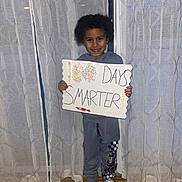 Grayson joined the competition — help win amazing prizes! child, smiling, sign, handmade, celebration, indoor, curtains, pajamas, socks, wood_floor, standing, happy, person, home, decor, text, 100_days, craft, cute, portrait