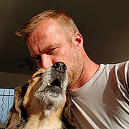 Leyka participe au concours pour gagner de l'argent avec cette photo : man, dog, face, close_up, indoor, natural_light, affection, pet, human, animal, companion, love, casual_clothing, short_hair, beard, smiling_dog, nose, whiskers, friendship, portrait