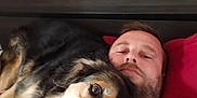 Leyka participe au concours pour gagner de l'argent avec cette photo : man, dog, bed, pillow, blanket, indoor, resting, lying_down, pet, canine, comfort, relaxation, red_bedding, head, face, fur, nose, close_up, domestic_animal, human