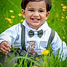 baby, bow_tie, casual_clothing, child, closeup, cute, daylight, grass, greenery, happy, nature, outdoor, portrait, sitting, smiling, suspenders, toddler, white_shirt, wildflowers, young_child