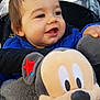 Enzo participe au concours pour gagner de l'argent avec cette photo : baby, child, smile, blue_jacket, stroller, plush_toy, mickey_mouse, toy, happy, face, hand, outerwear, blanket, cushion, person, cute, infant, indoors, portrait, closeup
