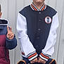 child, boy, backpack, naruto, anime, jacket, black, white, orange, standing, pose, young, casual_clothing, peace_sign, hand_gesture, short_hair, outdoor, concrete, wall, person
