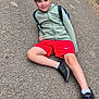 backward_cap, boy, cap, casual, child, daytime, gravel, greenery, hoodie, nature, outdoor, path, person, posing, recreation, red_shorts, relaxed, smiling, sneakers, young