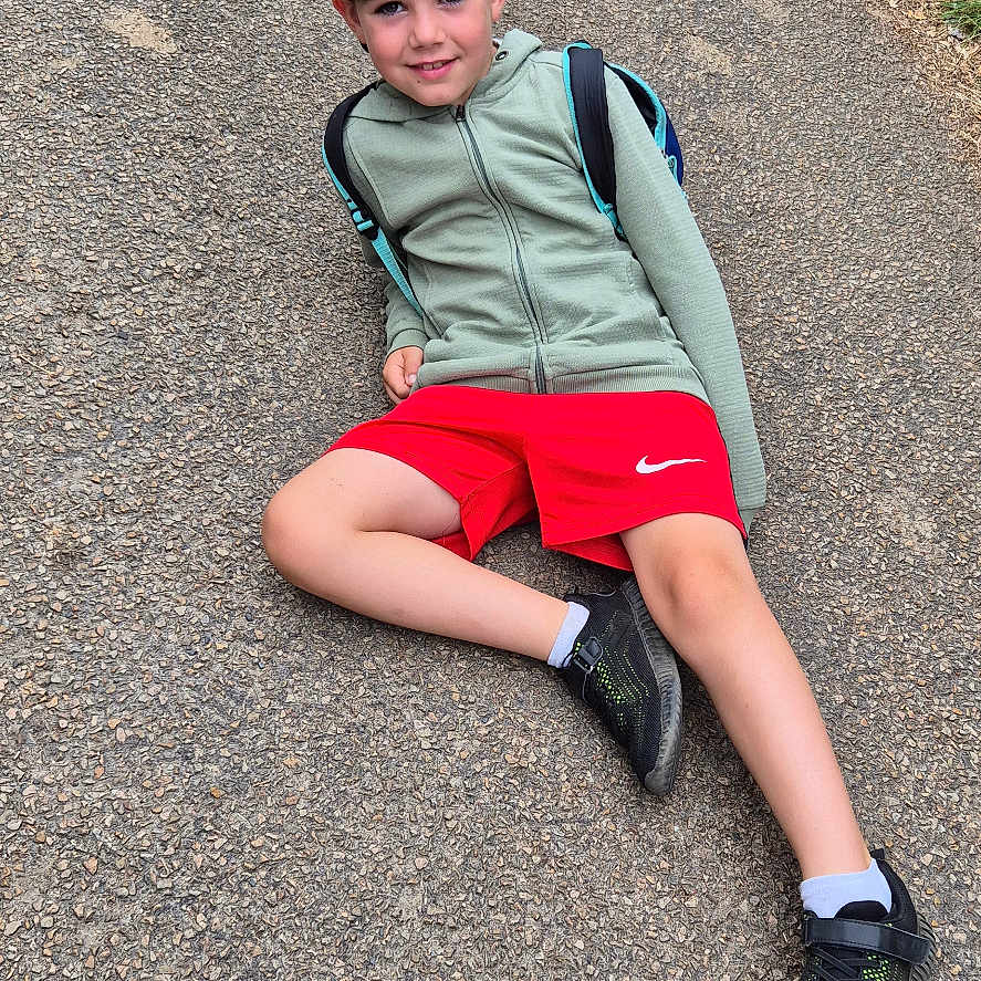 Enzo participe au concours pour gagner de l'argent avec cette photo : backward_cap, boy, cap, casual, child, daytime, gravel, greenery, hoodie, nature, outdoor, path, person, posing, recreation, red_shorts, relaxed, smiling, sneakers, young