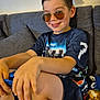 child, boy, sunglasses, smile, hair, couch, blanket, shorts, tshirt, indoor, casual, relaxed, furniture, person, seat, happy, portrait, hand, skin, home