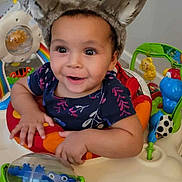 Lenayah is registered to the contest to win money with this photo: toddler, child, baby, bunny_ears, toy, activity_center, smiling, happy, indoor, playful, colorful, curly_hair, blue_shirt, plastic_toy, floor, carpet, cute, infant, person, expression