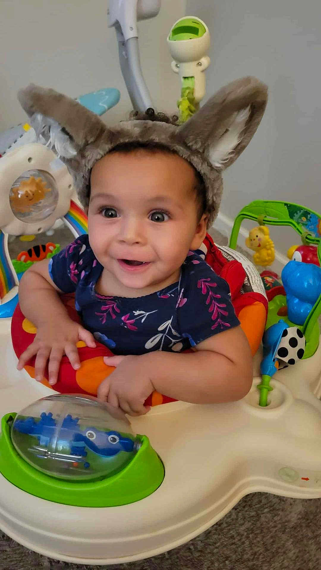 Lenayah is registered to the contest to win money with this photo: toddler, child, baby, bunny_ears, toy, activity_center, smiling, happy, indoor, playful, colorful, curly_hair, blue_shirt, plastic_toy, floor, carpet, cute, infant, person, expression