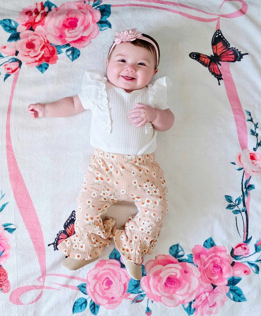 Laluna is registered to the contest to win money with this photo: baby, smiling, infant, floral_blanket, butterfly, white_top, ruffles, peach_pants, patterned_clothing, headband, flower_headband, cute, happy, lying_down, child, small_hands, small_feet, indoors, portrait, soft_lighting