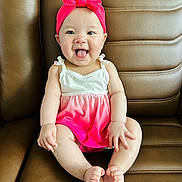 Chloe joined the competition — help win amazing prizes! baby, child, smiling, tongue_out, headband, pink_clothing, dress, sitting, leather_couch, happy, cute, infant, playful, indoors, person, skin, small_hands, small_feet, front_view, young
