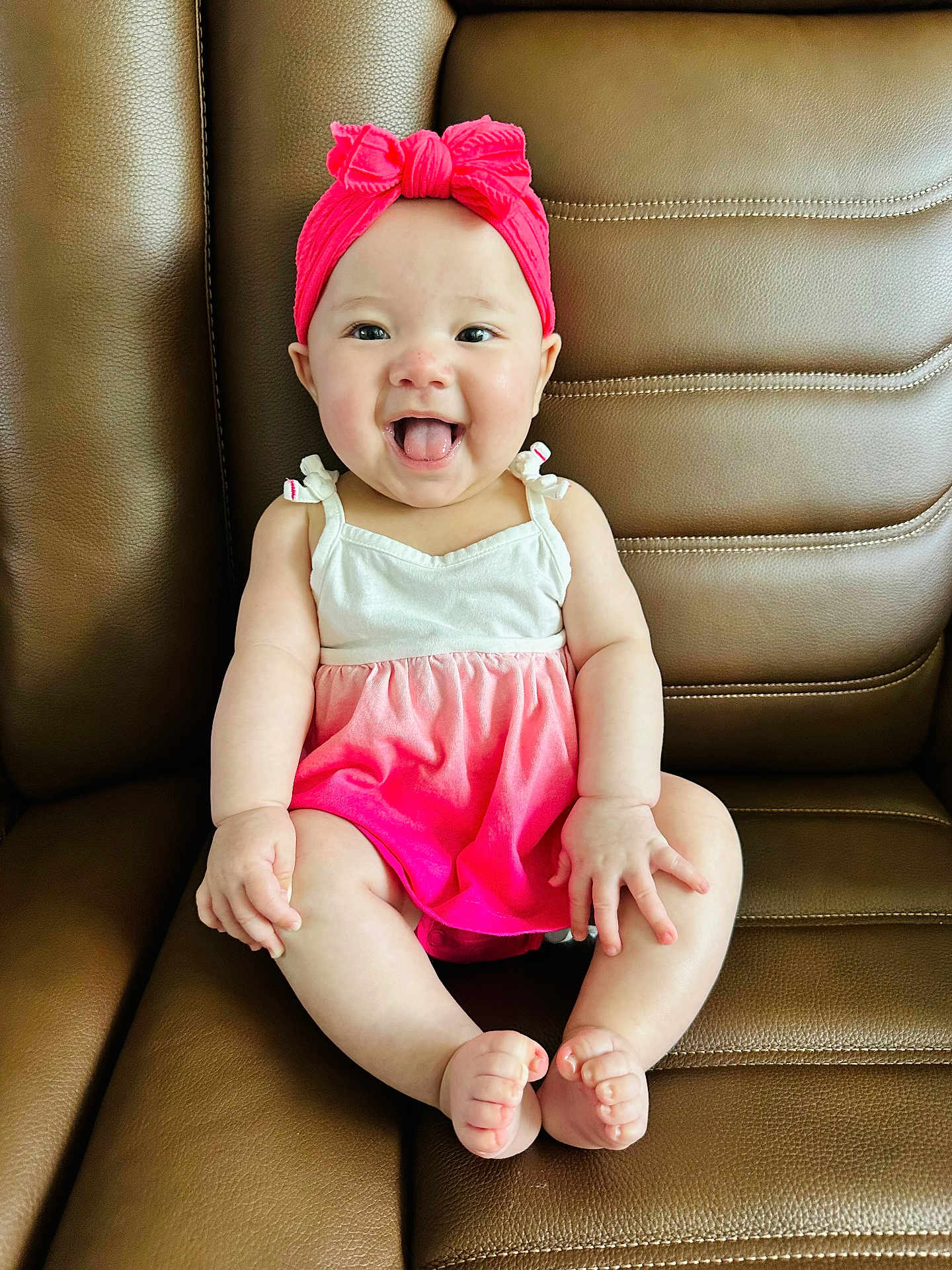 Chloe joined the competition — help win amazing prizes! baby, child, smiling, tongue_out, headband, pink_clothing, dress, sitting, leather_couch, happy, cute, infant, playful, indoors, person, skin, small_hands, small_feet, front_view, young