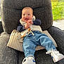 armchair, baby, casual, child, clothing, cushion, footwear, happy, indoor, jeans, pacifier, person, relaxing, smiling, sneakers, sunlight, toy, vest, window, wooden_beads