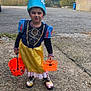 Anehyra participe au concours pour gagner de l'argent avec cette photo : child, costume, hat, face_paint, orange_basket, outdoor, gravel, shoes, dress, playful, smile, autumn, trees, building, sidewalk, person, toy_basket, fun, holiday, celebration