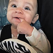 Kai is registered to the contest to win money with this photo: baby, child, face, hand, finger, car_seat, blanket, eyelashes, cute, infant, clothing, portrait, close_up, happy, chewing, seatbelt, soft_toy, smile, indoors, young_child