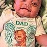 Kevion is registered to the contest to win money with this photo: baby, child, smiling, tshirt, portrait, angel_wings, halo, text, green_blanket, closeup, indoor, infant, person, face, happy, expression, lying_down, clothing, memorial, casual