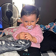 Opal is registered to the contest to win money with this photo: baby, pacifier, blanket, indoor, child, cute, smile, face, hands, clothing, fan, window, light, pink_stripes, black_pants, hair, person, sitting, cozy, playful